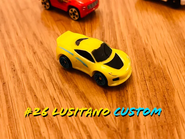 A carousel photo displaying the twenty-sixth vehicle named 'Lusitano Custom' out of an array of 'Deluxe Cars', at full size. The car is painted mostly yellow with the following components black; windshield, wheels, sides, bonnet and rear-windshield.