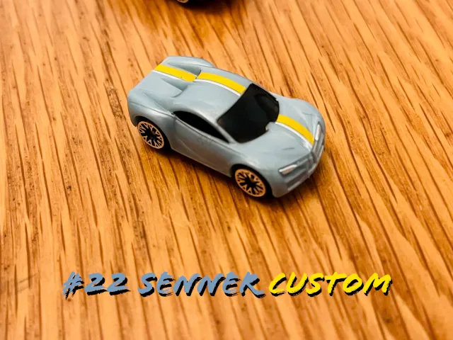 A carousel photo displaying the twenty-second vehicle named 'Senner Custom' out of an array of 'Deluxe Cars', at full size. The car is painted mostly grey with a single strike of yellow across the middle.