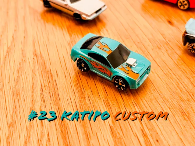 A carousel photo displaying the twenty-third vehicle named 'Katipo Custom' out of an array of 'Deluxe Cars', at full size. The car is painted mostly green with flames across the entire car like it's set on fire.