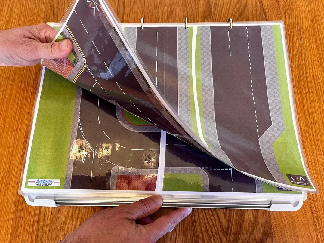 Fourth 'Compact & Convenient' carousel image with a hand flicking through the mini V.I.A. road layouts like it's a book.