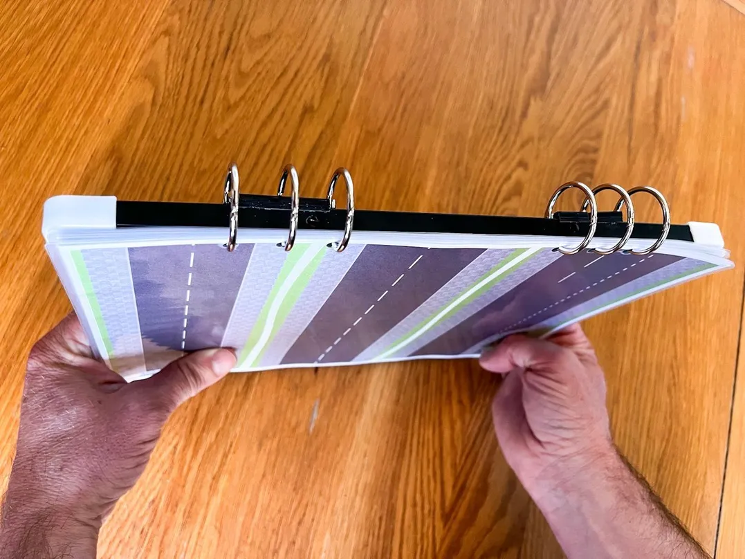 Ninth 'Compact & Convenient' carousel image with Julian demonstrating V.I.A. mini kit's ring binder holding the road layouts and board together.